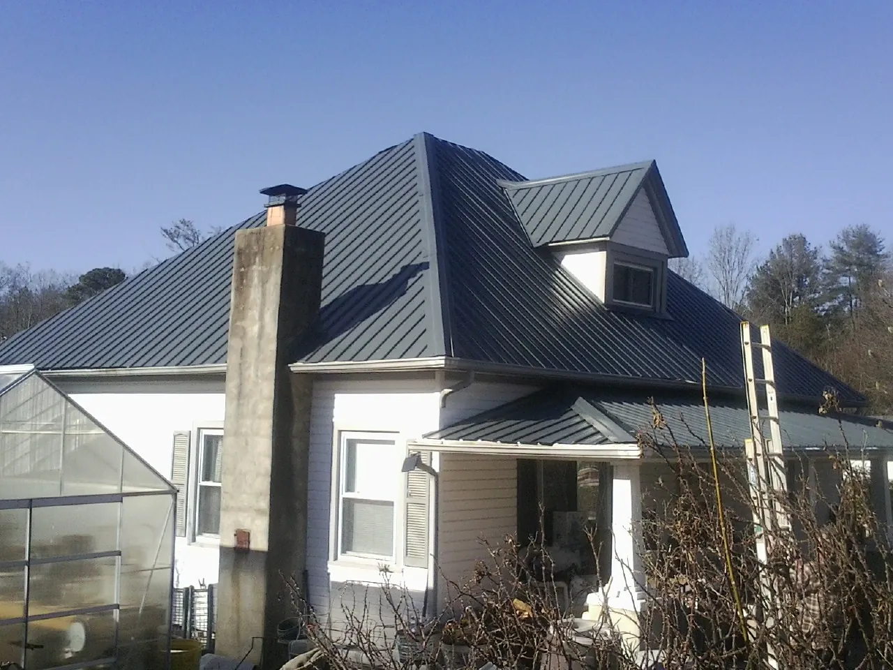 Dark blue standing seam metal roof on a white farmhouse with dormer — Slate & Tile Roof Repair by Roofing Brothers in Davilla
