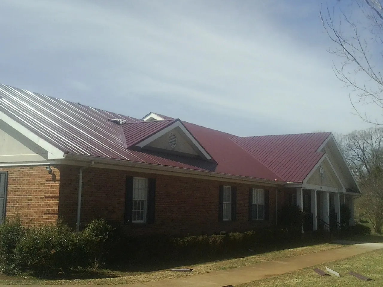 Red metal roof with gabled entries on a long brick building, from a Hail Damage Roof Repair job in Davilla
