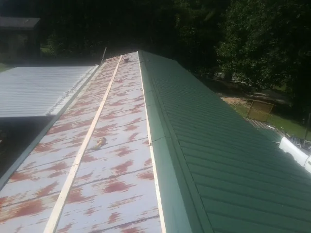 Old rusted panels beside newly installed green metal roofing — Wind Damage Roof Repair by Roofing Brothers in Davilla