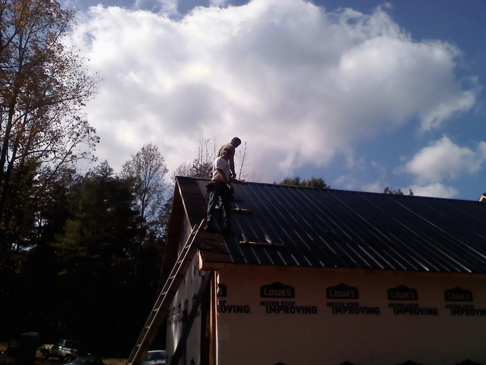 Roofer fastening dark metal panels high against a cloudy sky, from a Roof Inspection job in Davilla