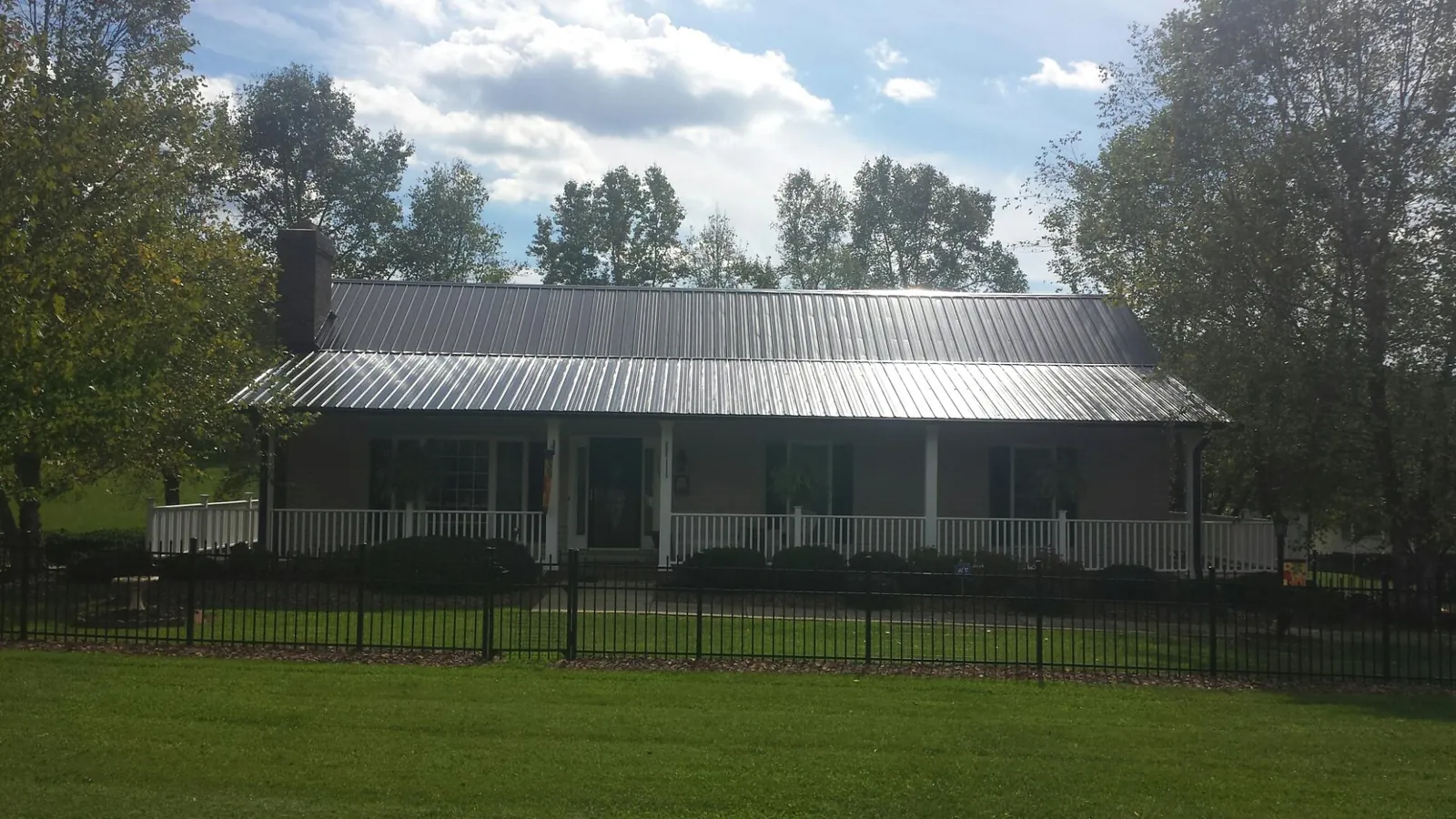 Gray metal roof on a brick ranch with a full width front porch — Gutter Guard Installation work by our crew in Davilla