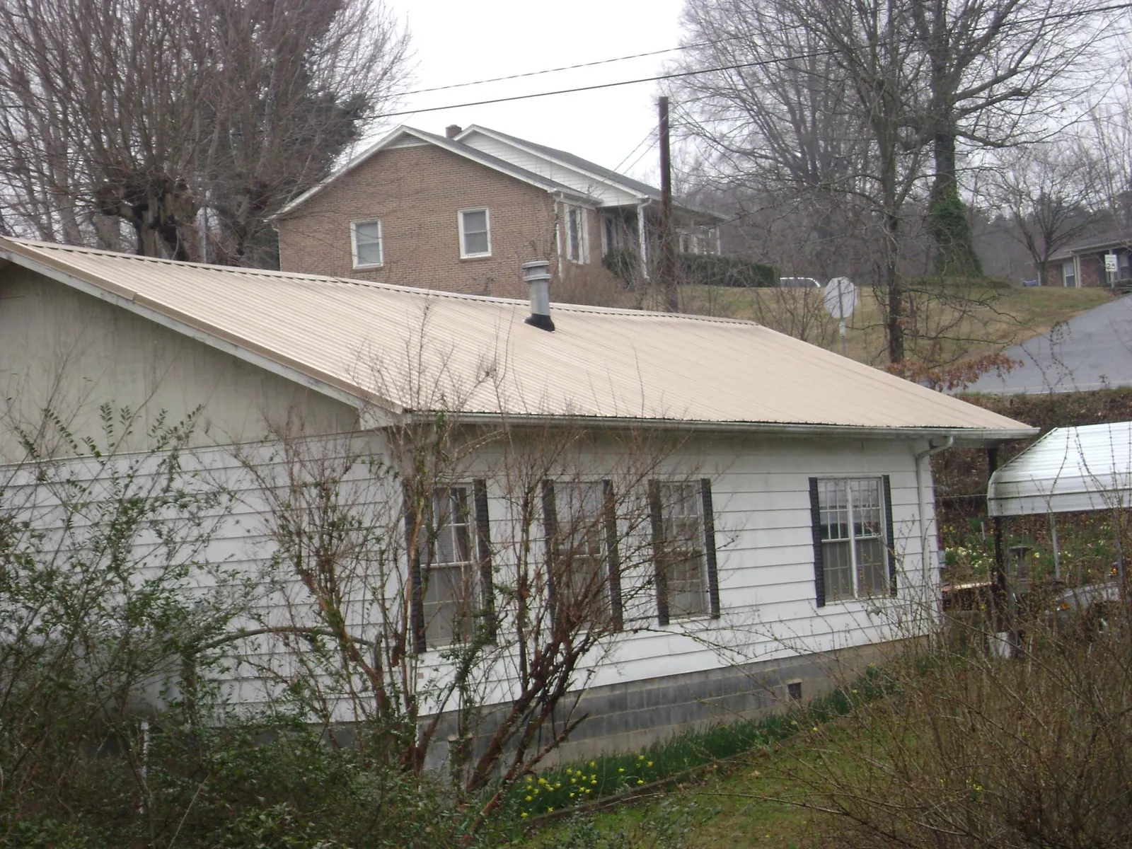 Tan metal roof on a white sided house set into a hillside — Commercial Roofing by Roofing Brothers in Davilla