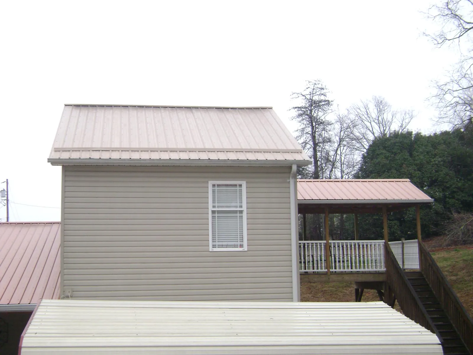 Tan metal roofs on a two story addition and attached porch, from a Roof Replacement job in Davilla