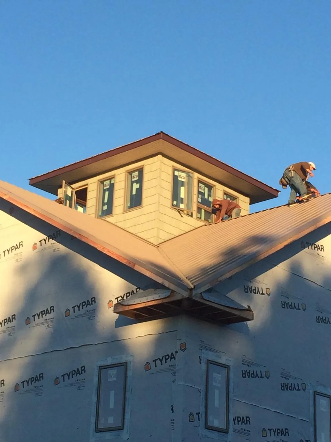 Roofers working around a rooftop cupola on a new metal roof at sunset — Roof Waterproofing in Davilla by Roofing Brothers
